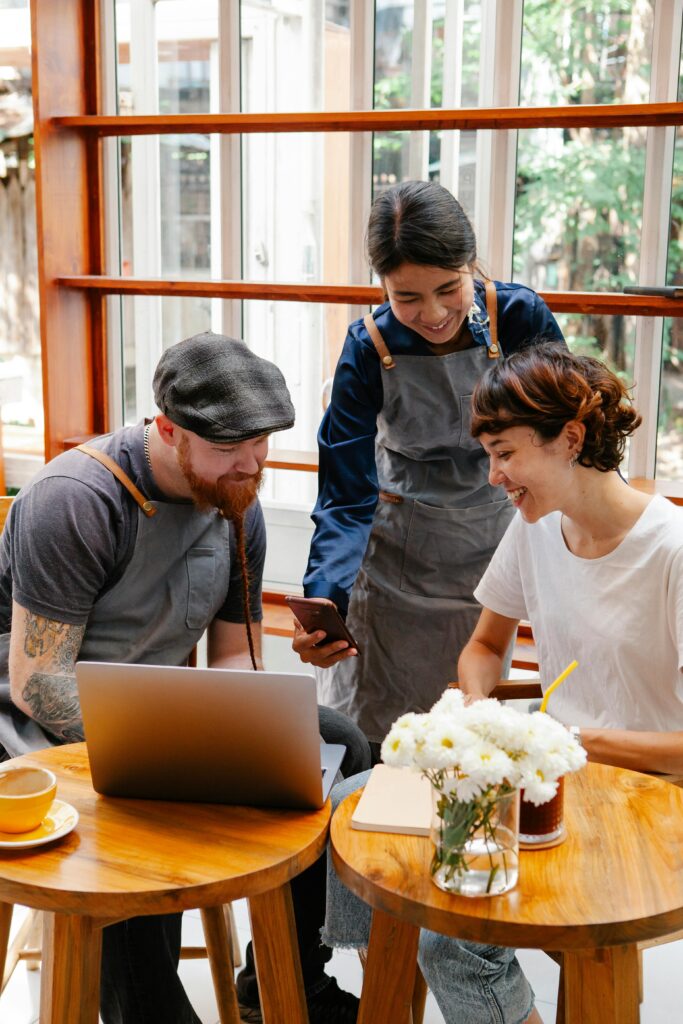 Three coworkers collaborate around a laptop in a sunny café.